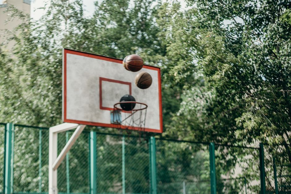 Basketball hoops with multiple balls flying in a green, outdoor park setting.
