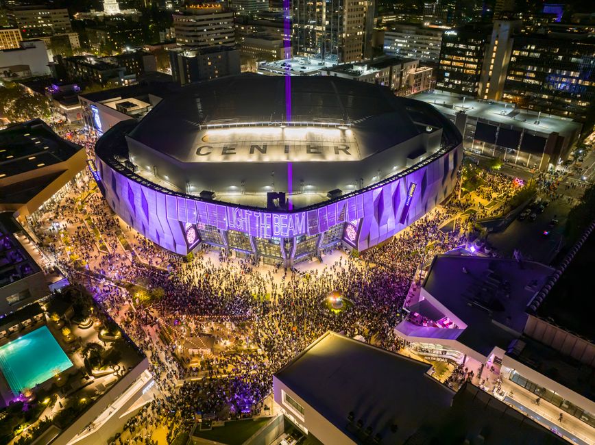 A vibrant night aerial view of Golden 1 Center in Sacramento, California during a lively event with a large crowd.