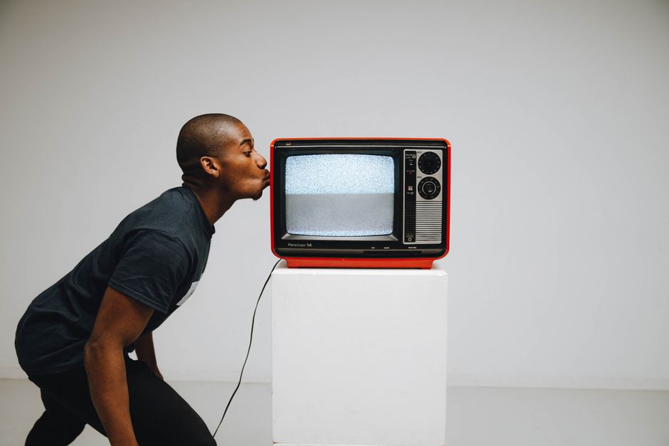 A man playfully kisses a vintage red television in a minimalist studio setting, evoking nostalgia and retro vibes.
