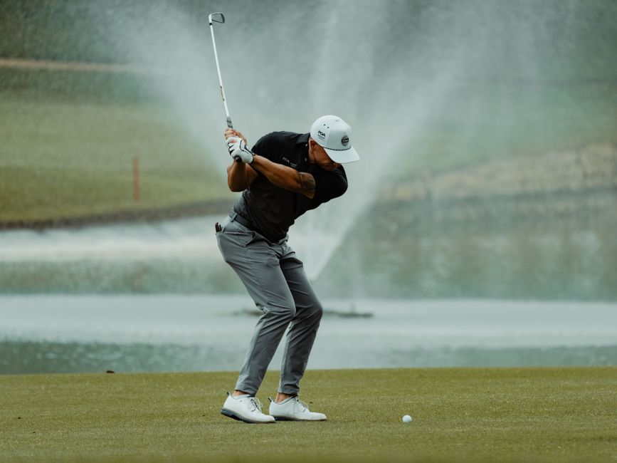 A golfer expertly swings his club on a lush green golf course with a fountain in the background.